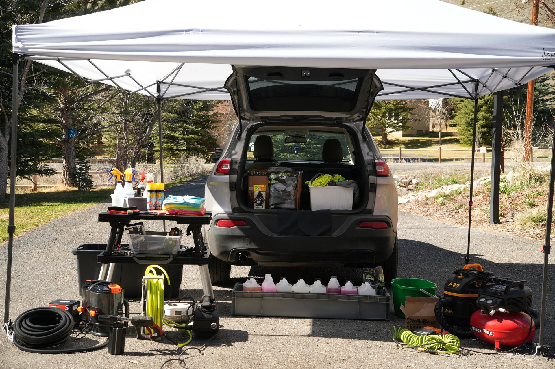Mobile detailing setup — open trunk with equipment under a pop-up canopy